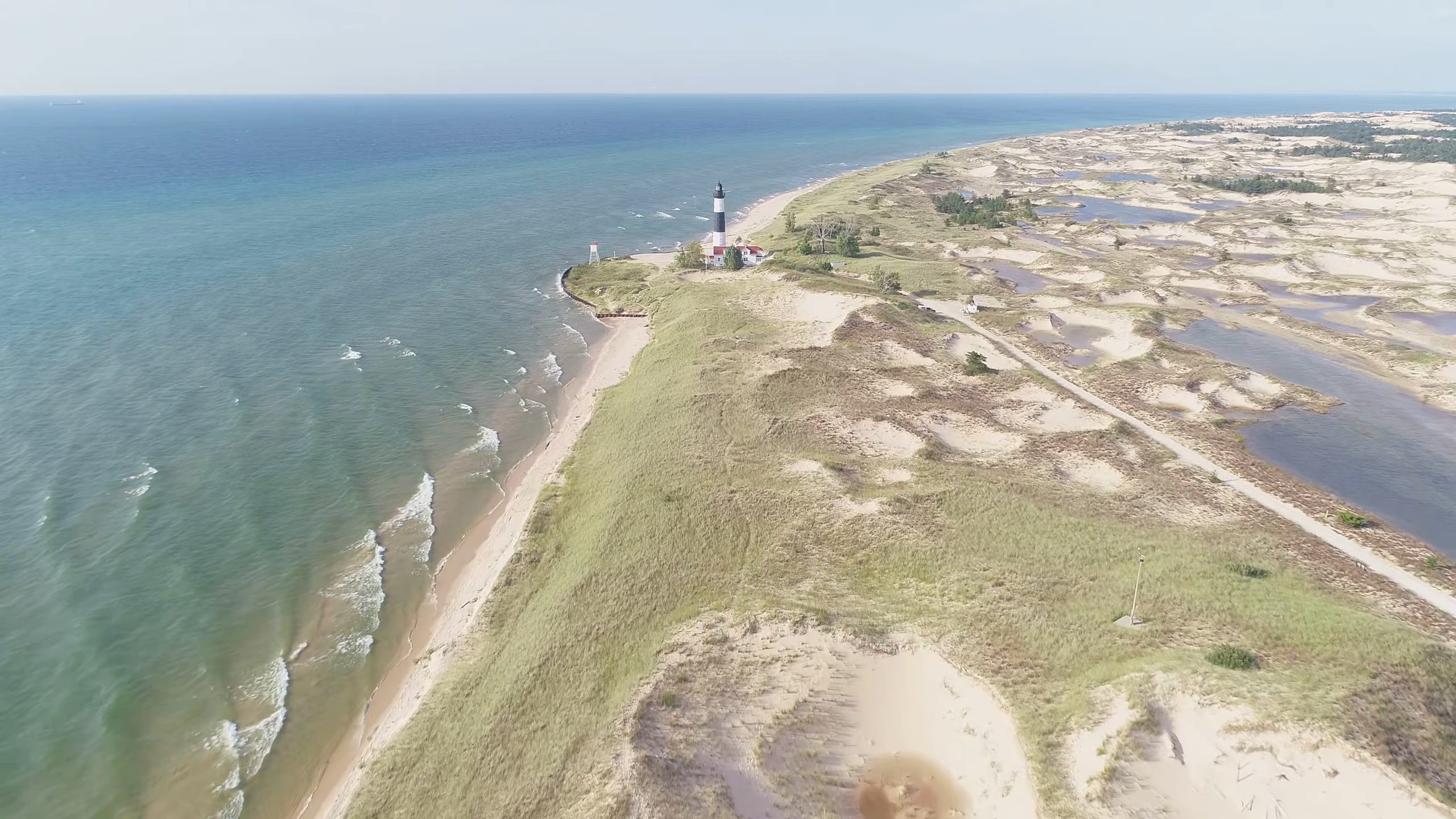 Aerial view of Big Sable Point Lighthouse, surrounded by sandy dunes, grassy terrain, and the vast waters of Lake Michigan