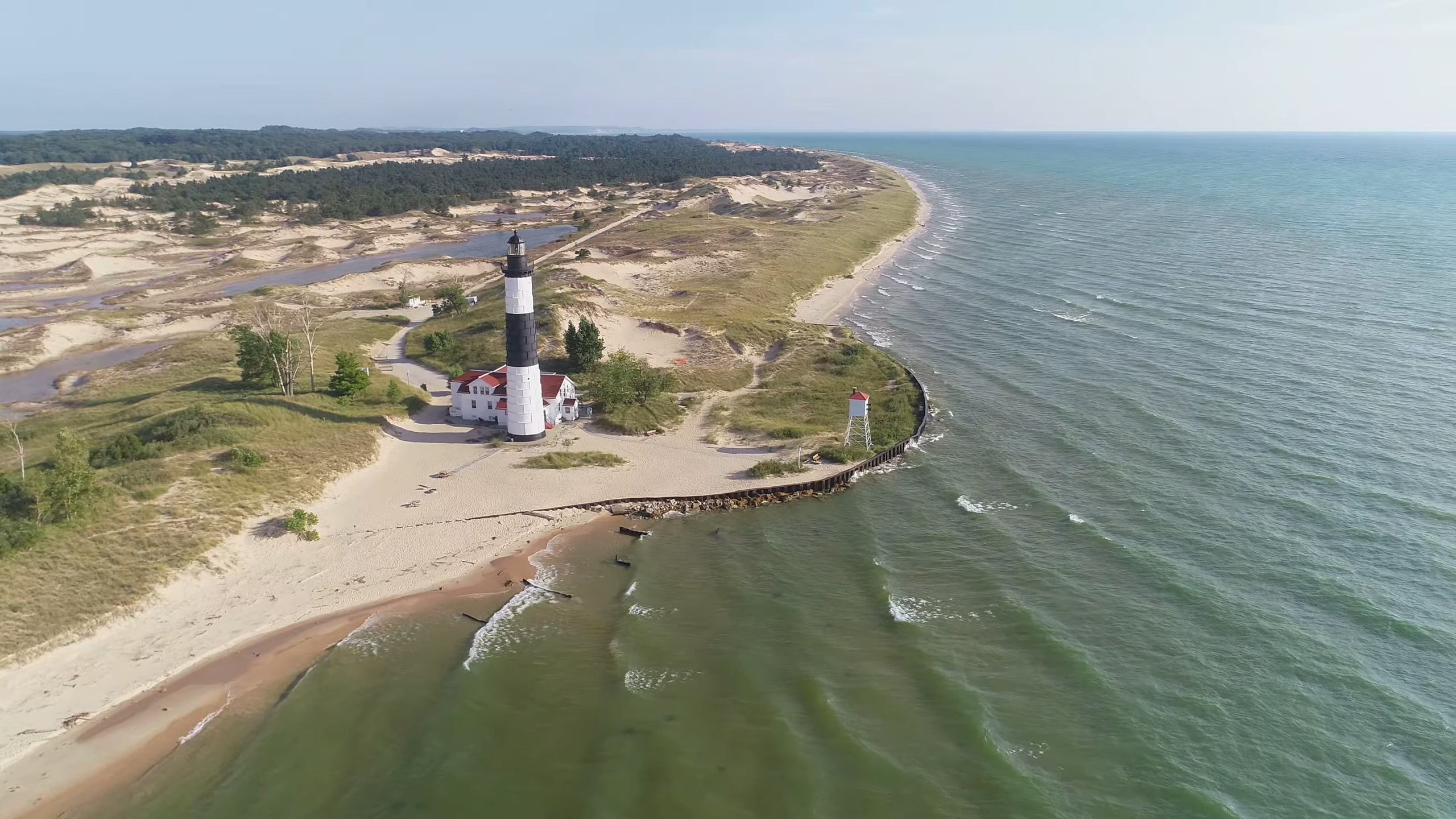 Aerial view of Big Sable Point Lighthouse with its black-and-white tower, surrounded by sandy dunes, grassy areas, and Lake Michigan's waters