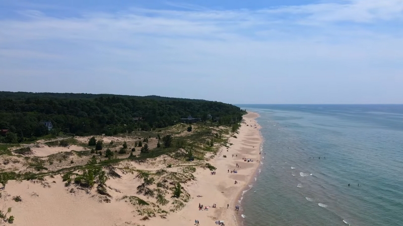 A View of The Silver Lake Sand Dunes with People Walking Along the Beach and The Lake in The Background