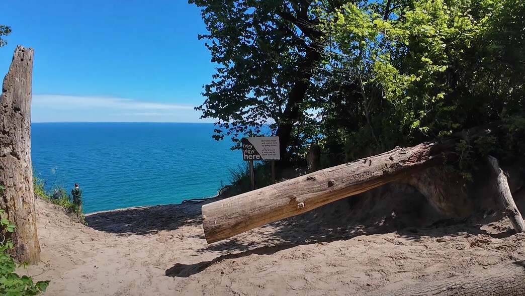 A sprawling log, a sandy path, and a breathtaking view of the vast blue lake